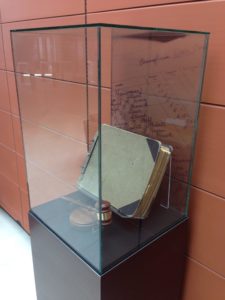 A glass case protecting the original ledger that  contains a page of signatures from 22 founding members of PSECU, as seen on the  print featured on the rear of the case.